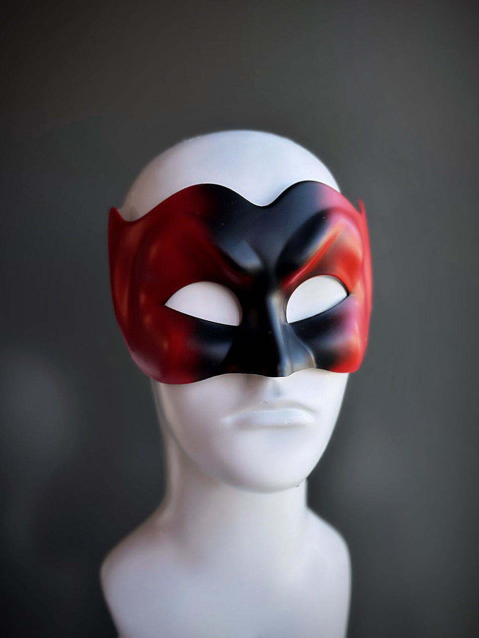 Venetian-style devil mask in black and red with a dramatic sculpted design, displayed on a mannequin.

