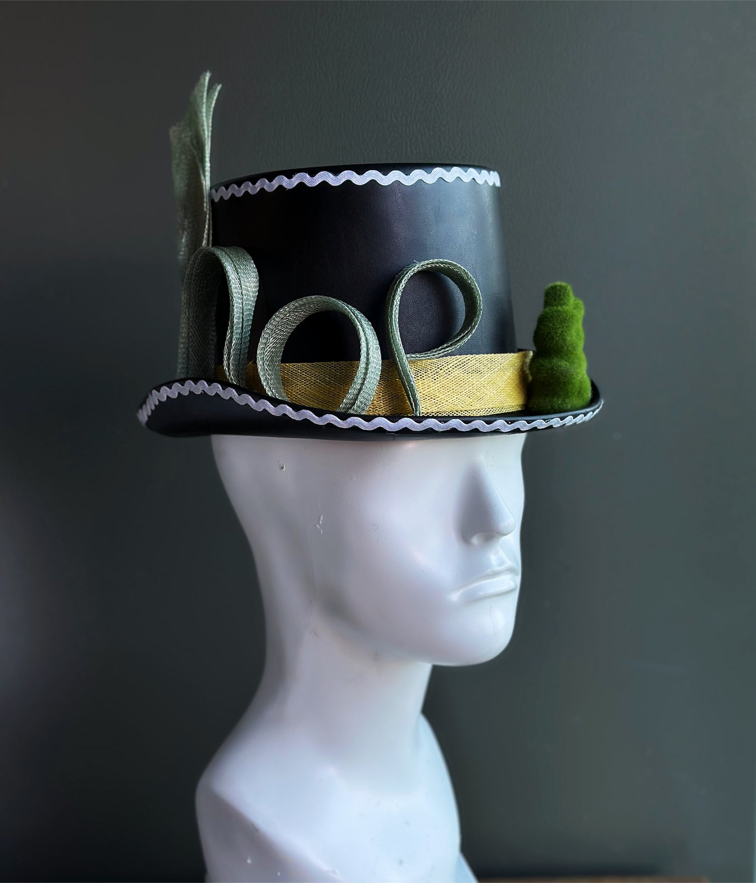 Whimsical black top hat with white trim, yellow sash around the head and green tulle design resting on the brim