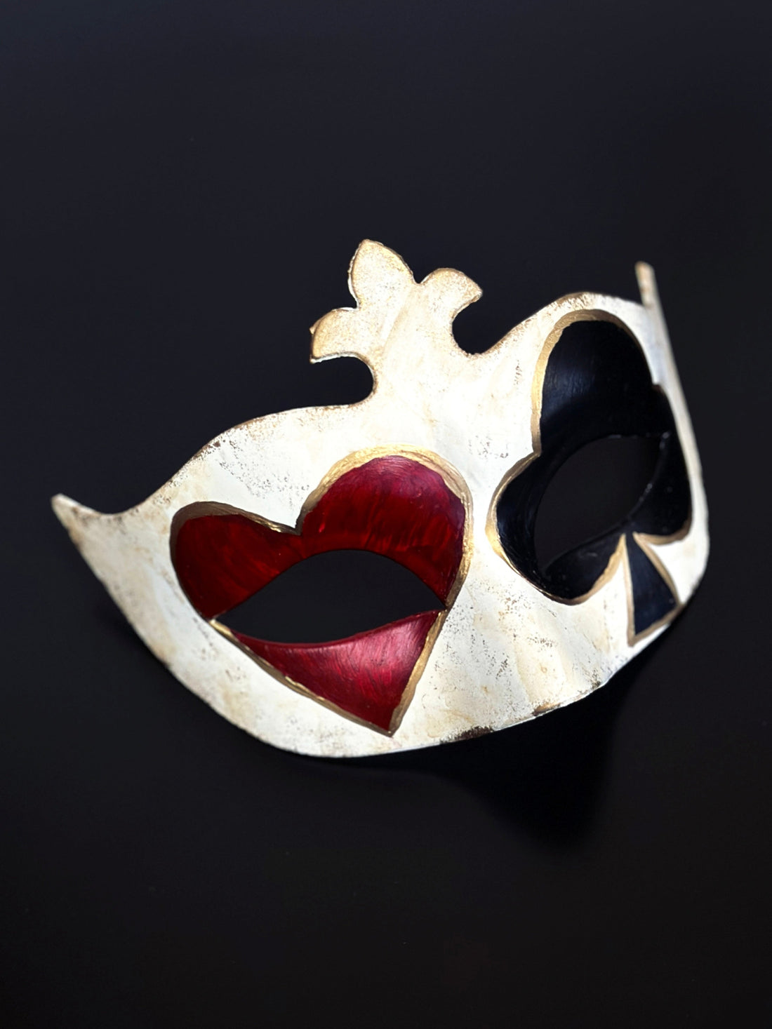 Red heart and black club card symbols over the eyes of a masquerade mask, with gold details.