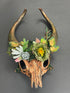 Fantasy woodland ram skull headdress featuring sculpted curved ram horns, faux flowers, moss, berries, and forest greenery. Ideal for Halloween, fantasy cosplay, Renaissance fairs, LARP, pagan festivals, woodland weddings, theatrical performances, fairy festivals, medieval events, and nature-inspired costume photography.