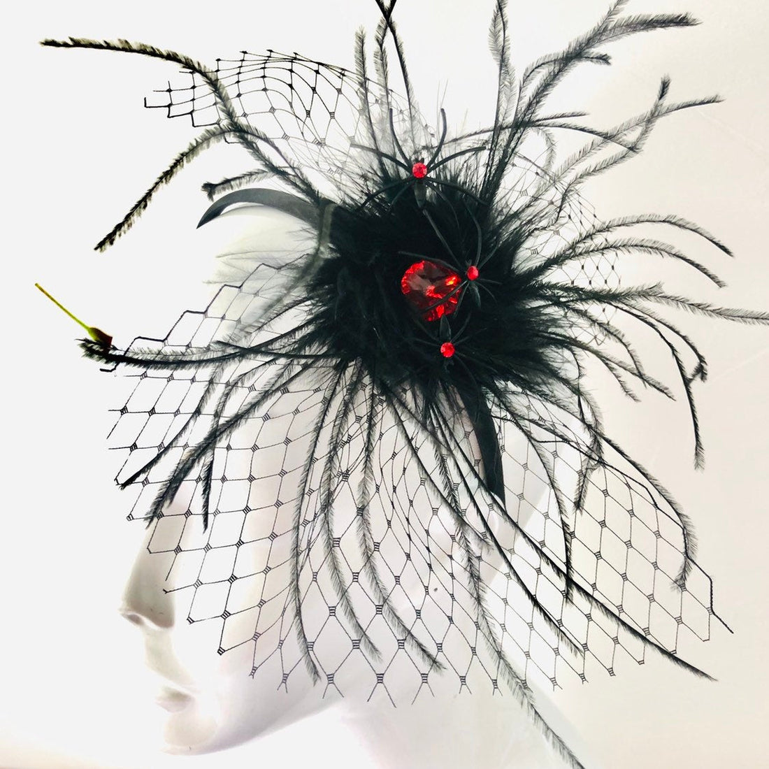 Feathered masquerade fascinator with net veil and red gemstone center